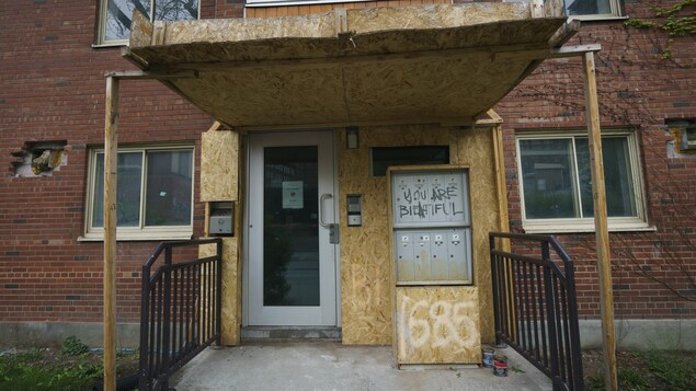 L'entrée d'un immeuble est à moitié barricadée et le mur de brique extérieur compte trois trous.