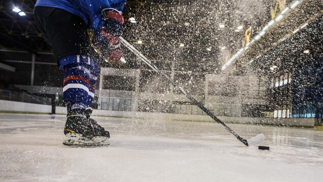 Un joueur de hockey propulse de la neige en freinant sur la glace.