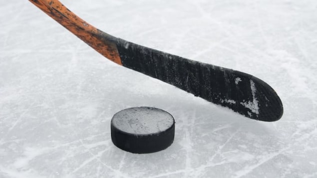 Un bâton de hockey et une rondelle sur la glace.