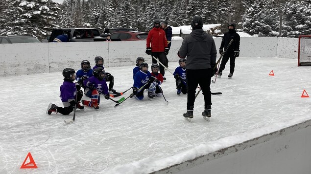 Des jeunes joueurs de hockey agenouillés sur une glace extérieure.
