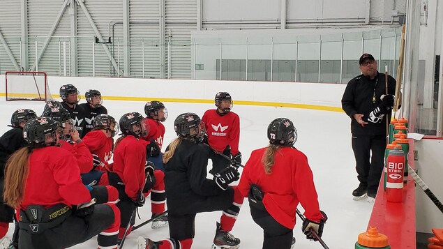Le groupe de hockeyeuse est rassemblé sur la glace près de l'entraineur pour recevoir ses conseils.