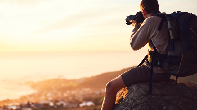 Un homme assis sur un rocher en train de photographier un coucher de soleil. Un homme assis sur un rocher en train de photographier un coucher de soleil.