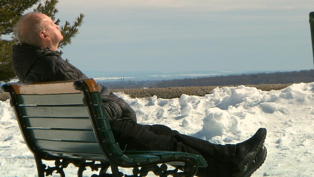 Un homme prend une pause au soleil sur un banc de parc des plaines d'Abraham à Québec, lors de la pandémie de coronavirus le 19 mars 2020