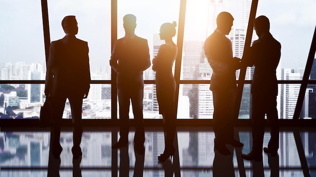 Des hommes et une femme d'affaires en contre-jour devant la fenêtre d'un immeuble de bureaux