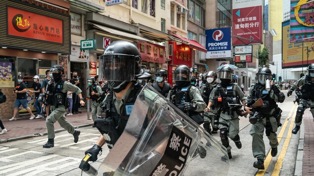 Les policiers courent au milieu de la rue, pendant que quelques piétons se serrent sur les devantures des magasins.