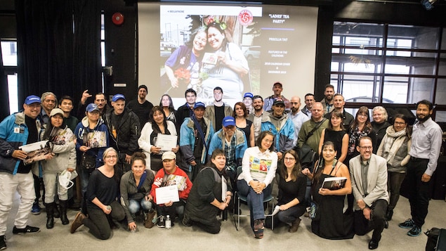 Une trentaine de personnes sourient avec en arrière-plan la photo gagnante du calendrier Hope in Shadows 2018 Une trentaine de personnes sourient avec en arrière-plan la photo gagnante du calendrier Hope in Shadows 2018