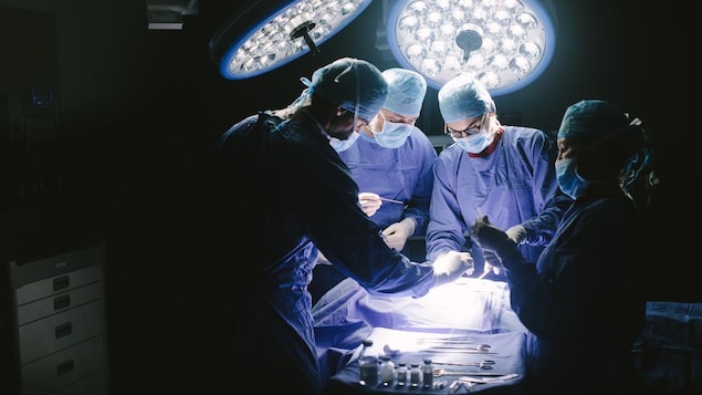Vue générale d'une salle d'opération avec quatre membres d'une équipe médicale à l'oeuvre.