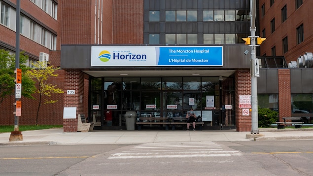 Une personne assise sur un banc devant l'Hôpital de Moncton.