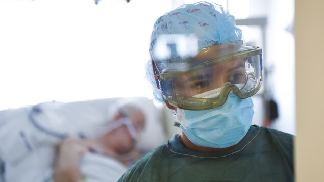 Une infirmière porte des lunettes de protection et un masque.