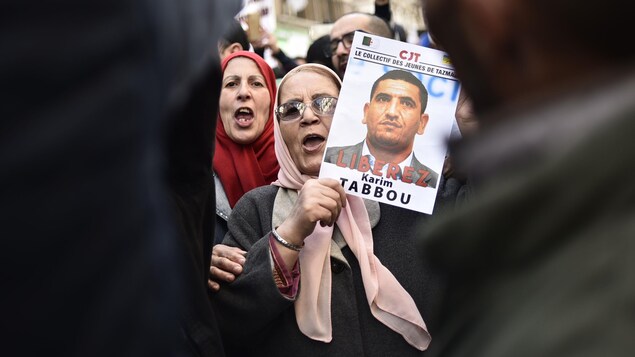 Une femme au milieu de manifestants portant le portrait de Karim Tabbou.