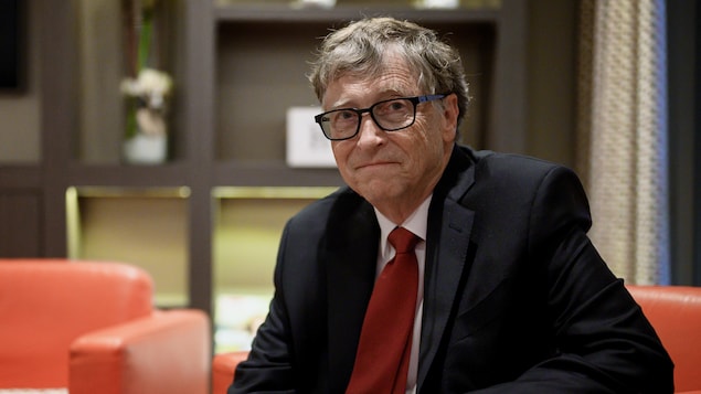 Bill Gates, assis sur un divan, regarde la caméra.