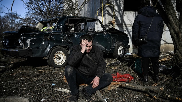 2022 年 2 月 24日：一个男子蹲在自己在楚吉夫 （Chuguiv ）市被炮弹摧毁的住所大楼外。