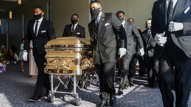 Des hommes noirs tirent son cercueil doré. 