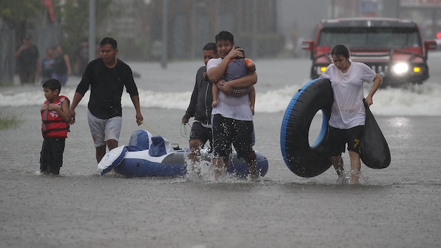 Un groupe de sinistrés marchent dans une rue inondée.