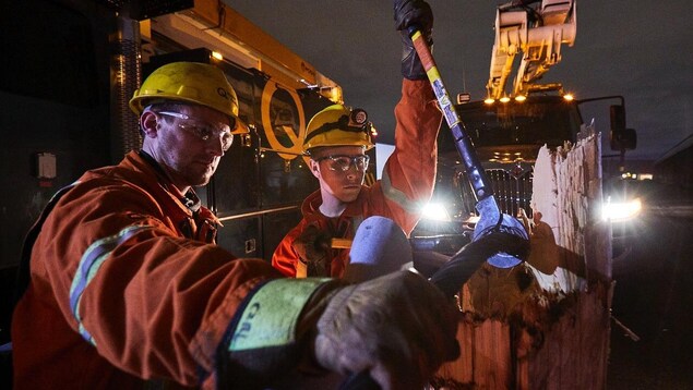 Deux travailleurs d'Hydro-Québec réparent un poteau endommagé par les intempéries, à l'aube.