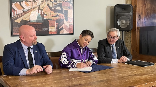 Trois personnes assises à une table signent un document.