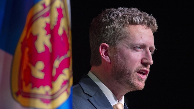 L'homme prononce un discours devant un drapeau de la Nouvelle-Écosse.