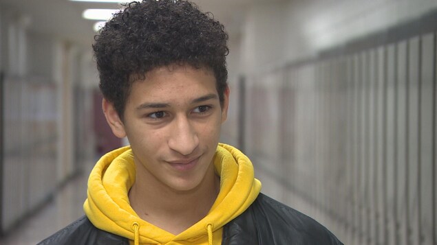 Portrait d'un jeune adolescent aux cheveux noirs bouclés coupés courts qui esquisse un sourire en écoutant attentivement la journaliste. Portrait d'un jeune adolescent aux cheveux noirs bouclés coupés courts qui esquisse un sourire en écoutant attentivement la journaliste.