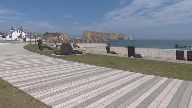 Des touristes sont assis sur des chaises longues ou se promènent sur une plage devant le rocher Percé.