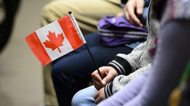 Une jeune personne immigrante tient un petit drapeau du Canada lors d'une cérémonie de citoyenneté à Ottawa, sur la colline du Parlement, le 17 avril 2019.