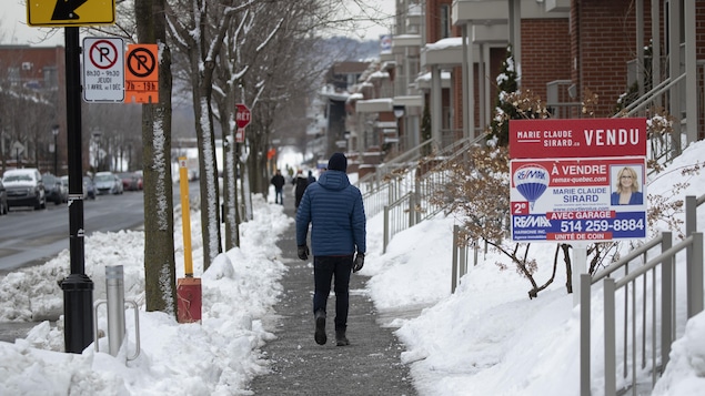 Un homme marche sur le trottoir devant une propriété marquée « vendue ».