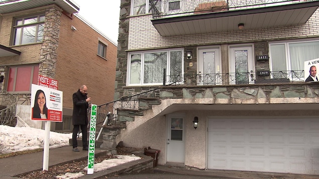 Un agent immobilier pose une pancarte de visite libre devant un triplex. Un agent immobilier pose une pancarte de visite libre devant un triplex.