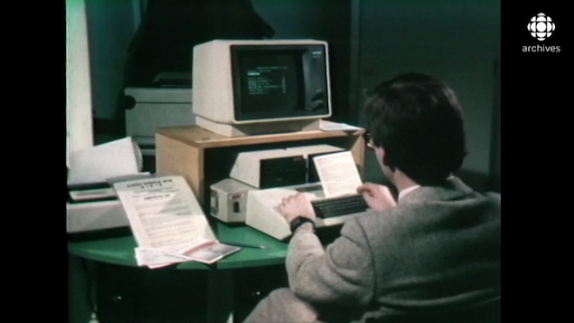 Homme, de dos, qui travaille avec un ordinateur à l'allure ancienne. 