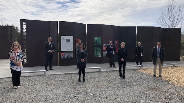 Des représentants de Saguenay et de l'organisation des commémorations posent devant le monument rendant hommage aux victimes du glissement de terrain.