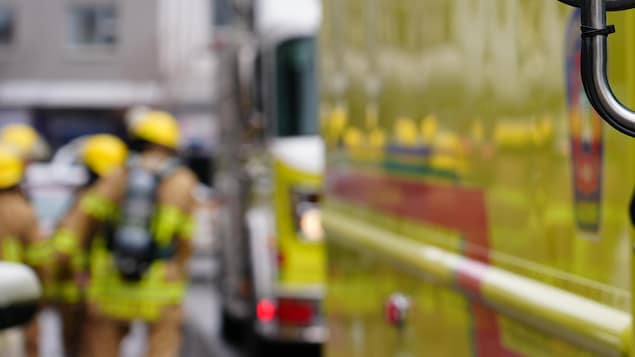 Trois pompiers en uniforme se déplacent près de deux de leurs camions.