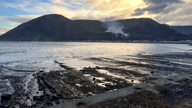 Un feu et de la fumée dans une montagne, près de village en bord de mer.