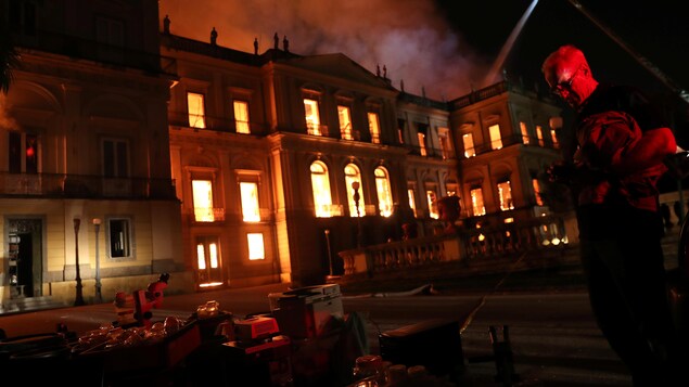 Un homme porte des objets devant le bâtiment en flamme.