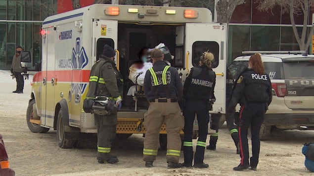 Des ambulanciers installent la civière dans une ambulance, sous la surveillance d'une policière. 