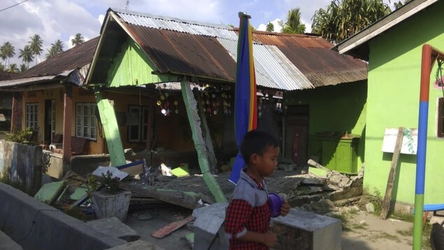 Un garçon devant une maison détruite.