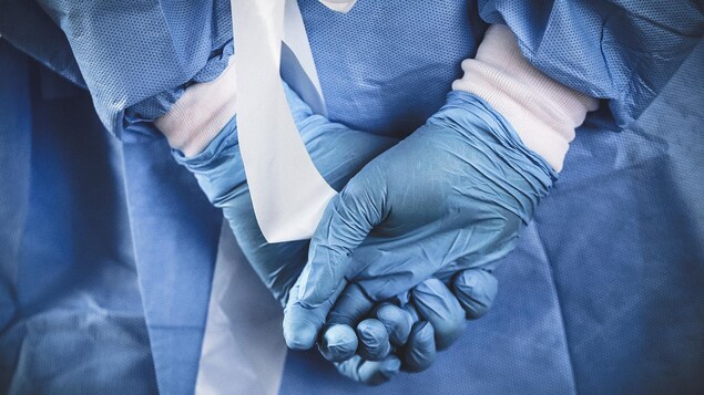 Une infirmière qui porte des gants de caoutchouc joint se mains derrière son dos.