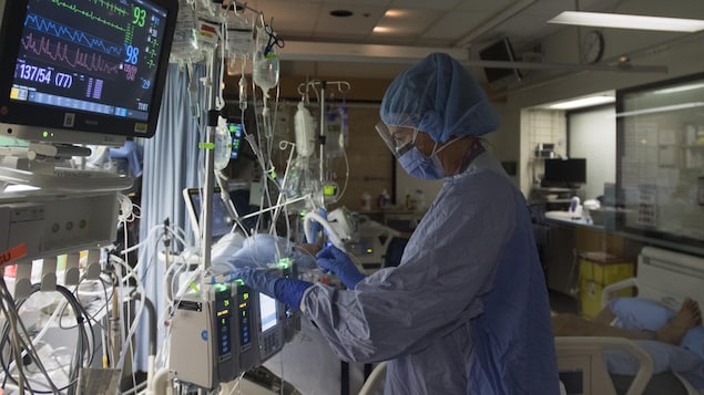 Une infirmière dans un hôpital, à côté d'un patient sous aide respiratoire.