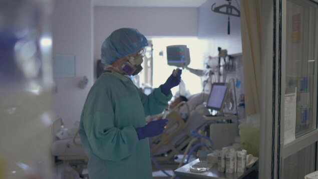Une infirmière porte un masque, des gants et un équipement protecteur.