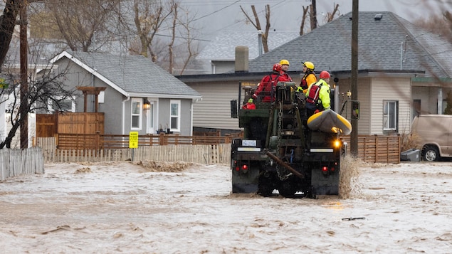 Les interventions d'urgence sont illustrées en train de conduire un camion dans les Des personnes sur un véhicule tout terrain dans une rue inondée, bordée de maisons. 