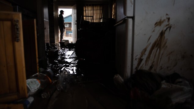 Un homme dans le cadre de la porte de sa maison, saccagée par les eaux.