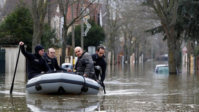 Des secouristes à bord d'un canot pneumatique naviguent sur une rue inondée. Des secouristes à bord d'un canot pneumatique naviguent sur une rue inondée.