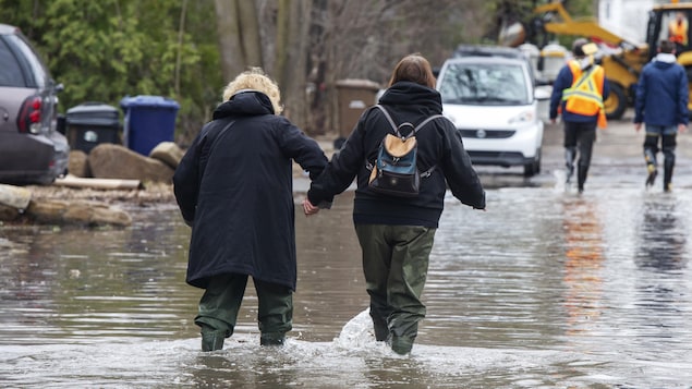 Des résidentes de Laval marchent dans une rue inondée.