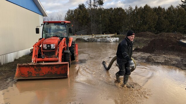 Un homme tient un tuyau alors qu'il marche sur le sol inondé à New Richmond, le 3 décembre 2020.