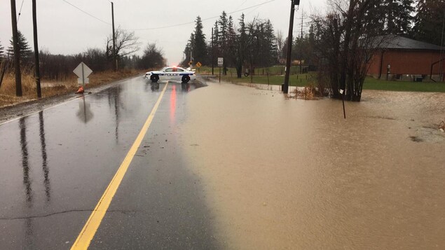Une rue inondée et une voiture de police au loin bloquant accès à la route.