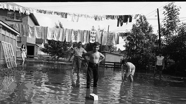 Une photo en noir et blanc où l'on voit une famille, les deux pieds dans l'eau.