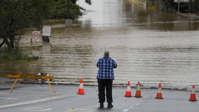 Un homme se tient devant une rue fermée et complètement inondée.