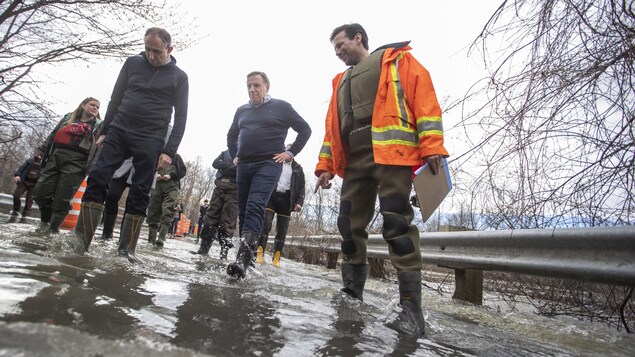 François Legault marche dans l'eau avec des bottes.