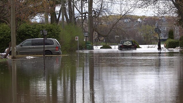 Une voiture stationnée dans une entrée de garage et un autre véhicule stationné au bout d'une rue sont entourées d'eau