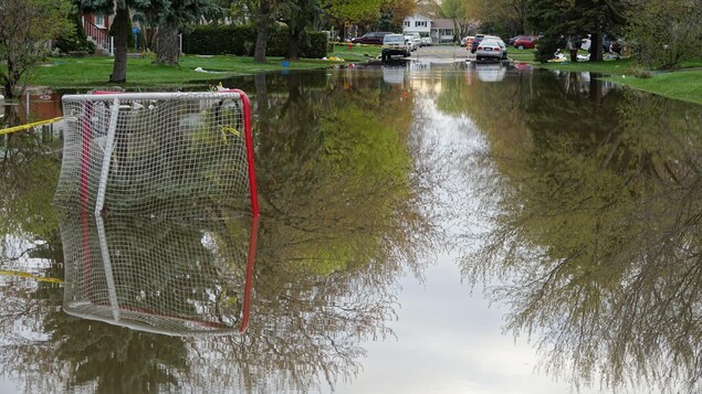 Une rue de Pierrefonds inondée, où l'on aperçoit un filet de hockey, des barrières et des voitures