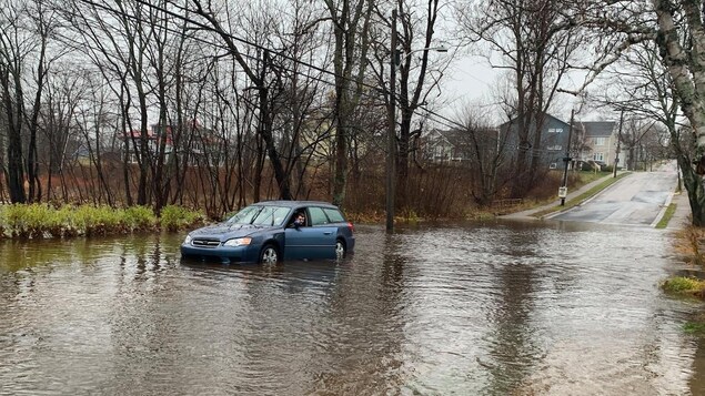 La voiture d'un homme est immobilisée dans l'eau sur une rue complètement inondée et il ouvre sa portière.