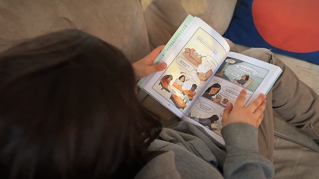 Un enfant regarde un livre assis sur un divan.
