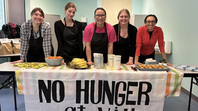 Cinq femmes derrière une table avec des aliments disposés dessus.